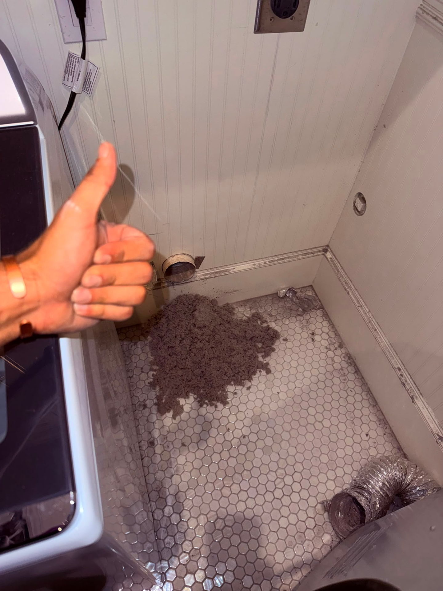Technician pointing to the cleaned dryer vent opening with the removed lint and debris collected on the laundry room floor