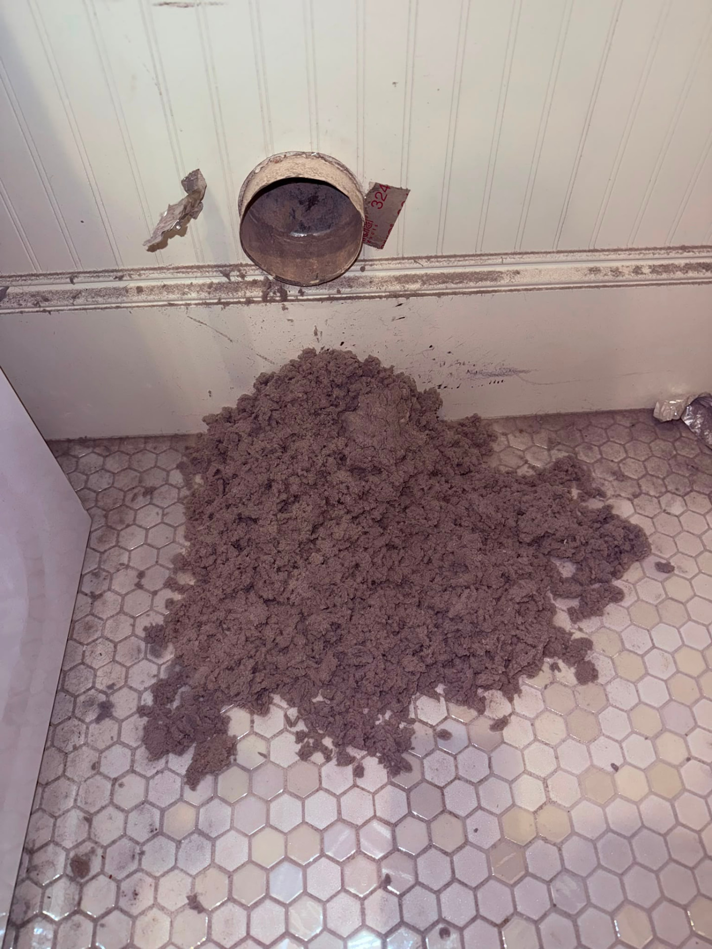 Pile of lint and debris removed from a dryer vent, on the laundry room floor beside the open wall vent connection