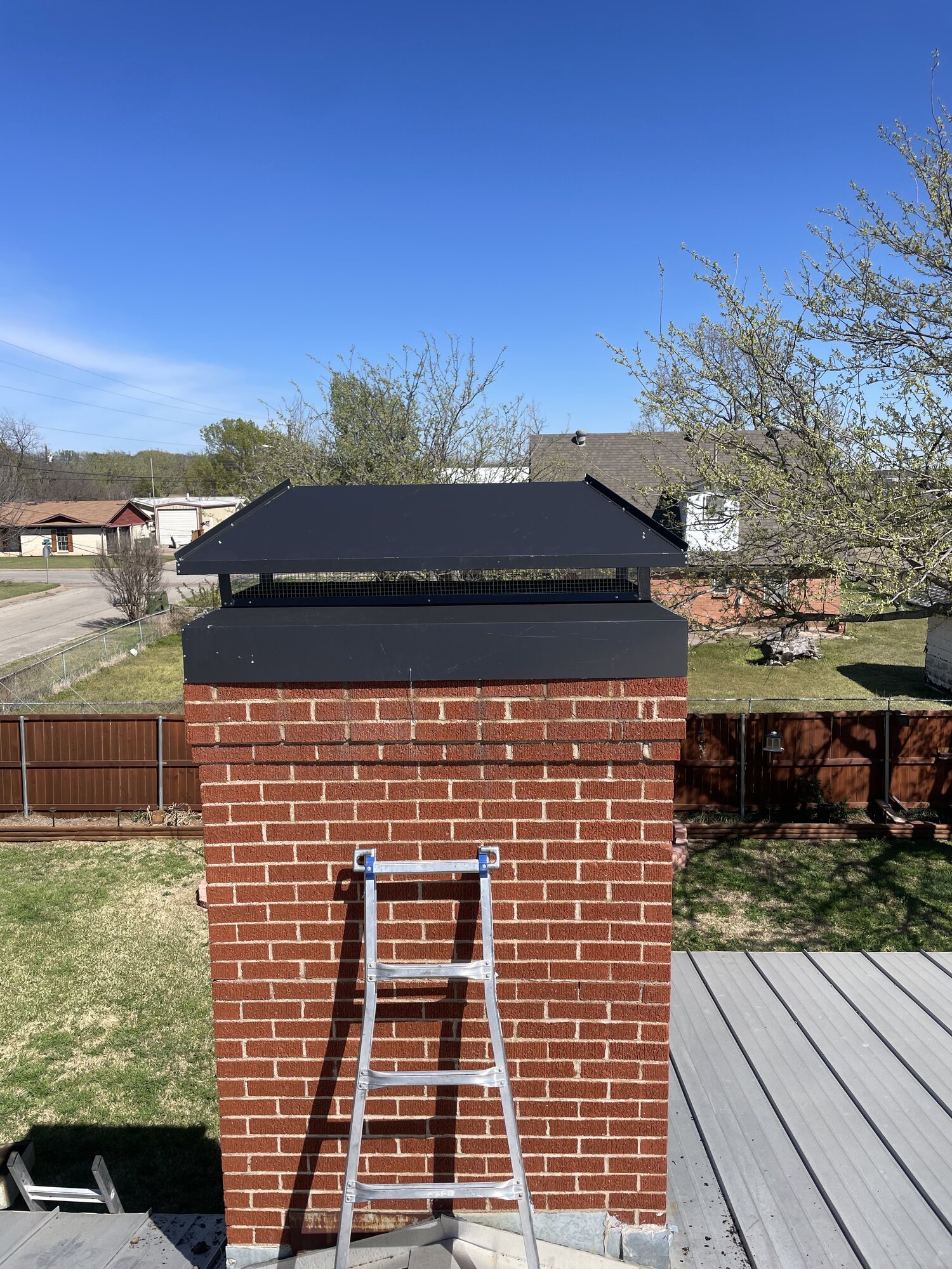 Completed new black chimney cap installation with mesh screen and matching crown surround on the brick chimney