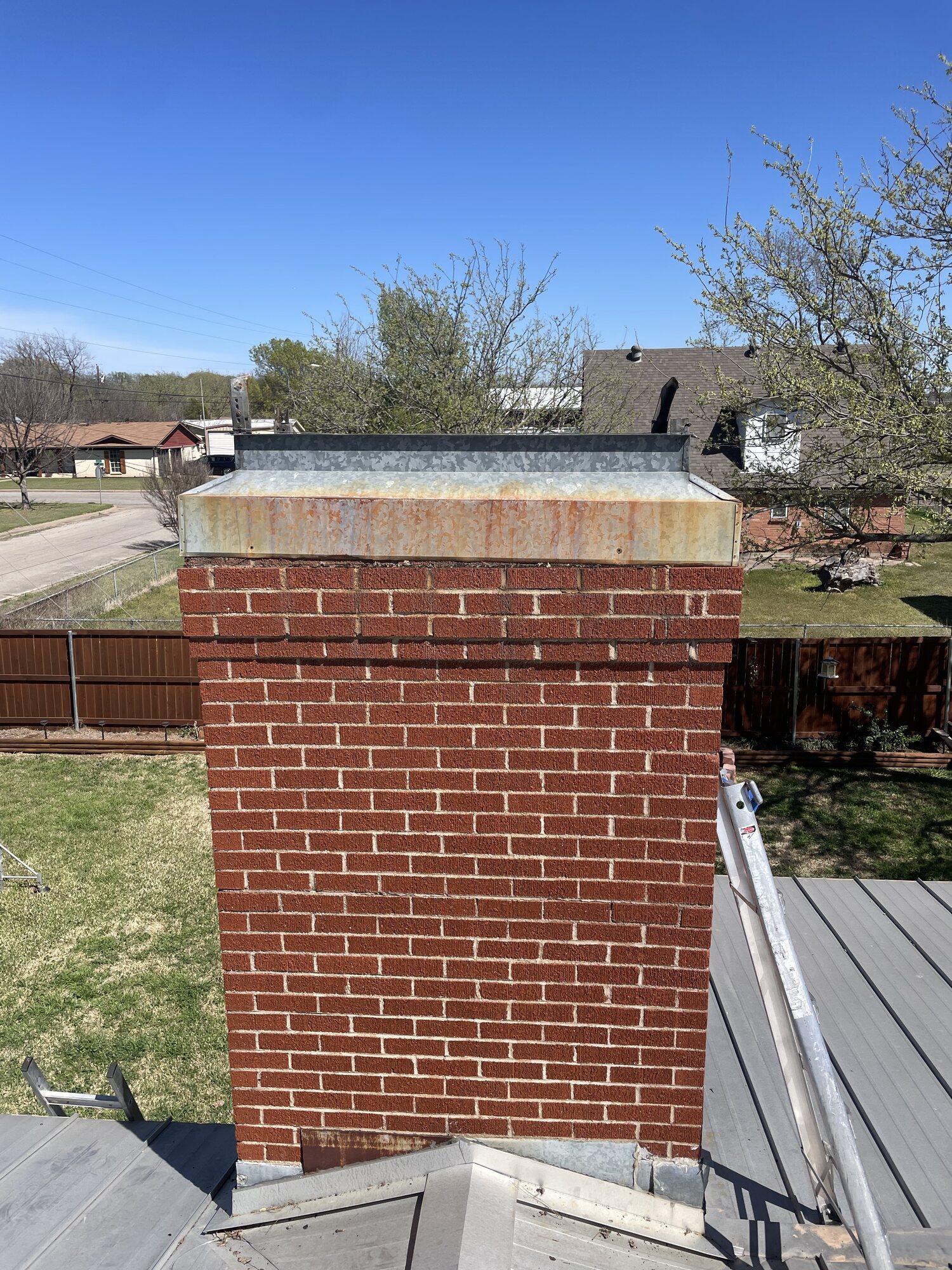 Original weathered galvanized chimney cap with rust staining sitting on the brick chimney crown before replacement