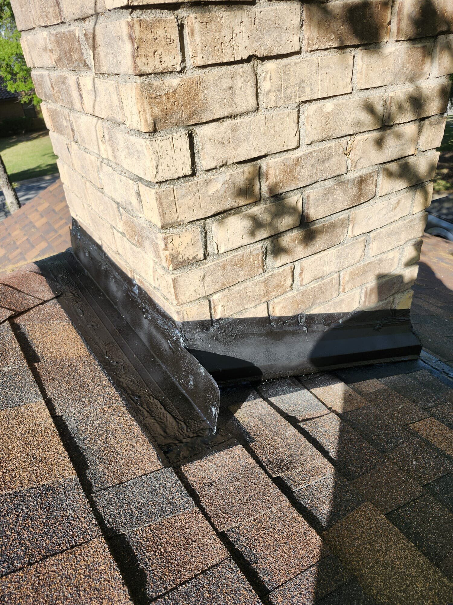 Existing chimney base flashing at the roofline showing aged sealant, gaps and weathered brick before the flashing work