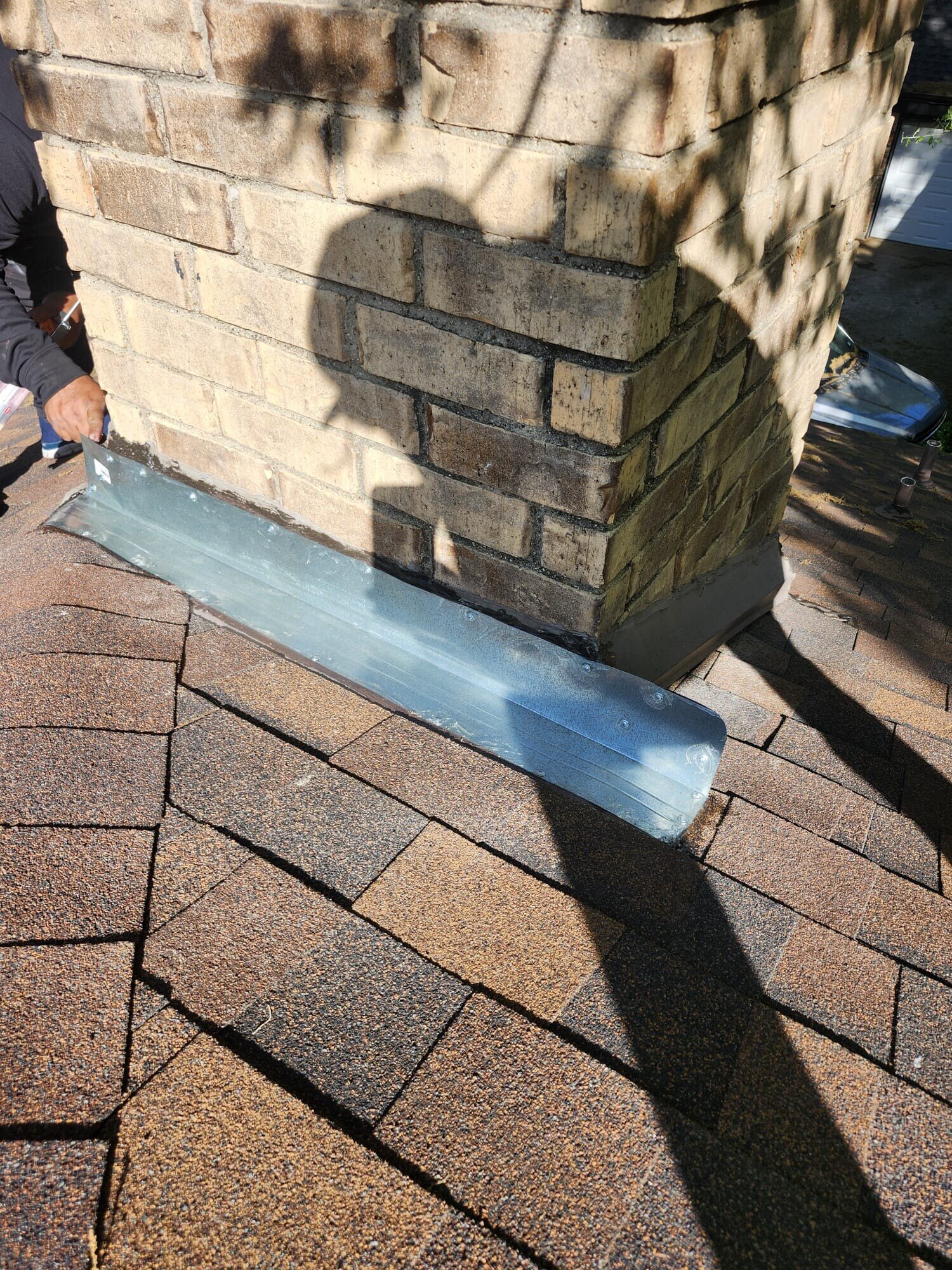 New galvanized step flashing section being set against the chimney brick and shingles during installation