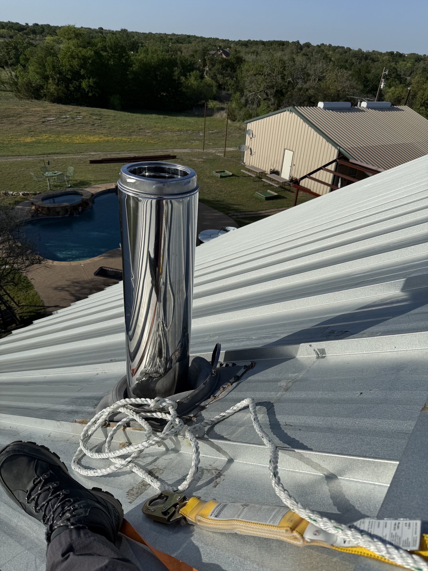 Roof-level detail of the metal flue pipe during service, with safety rope and harness equipment visible on the metal roof