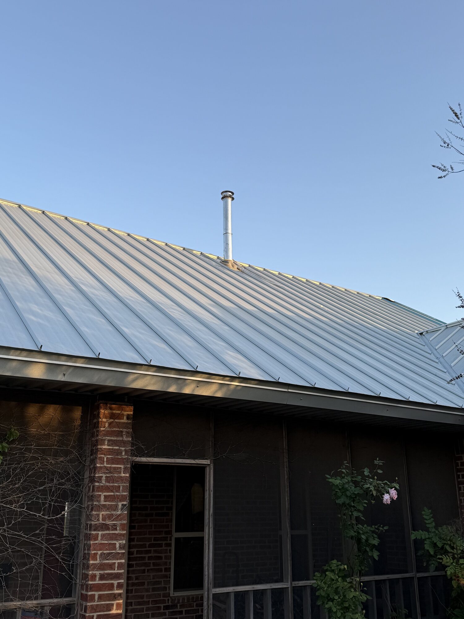 Exterior overview of a metal flue pipe extending through a standing-seam metal roof on a brick house