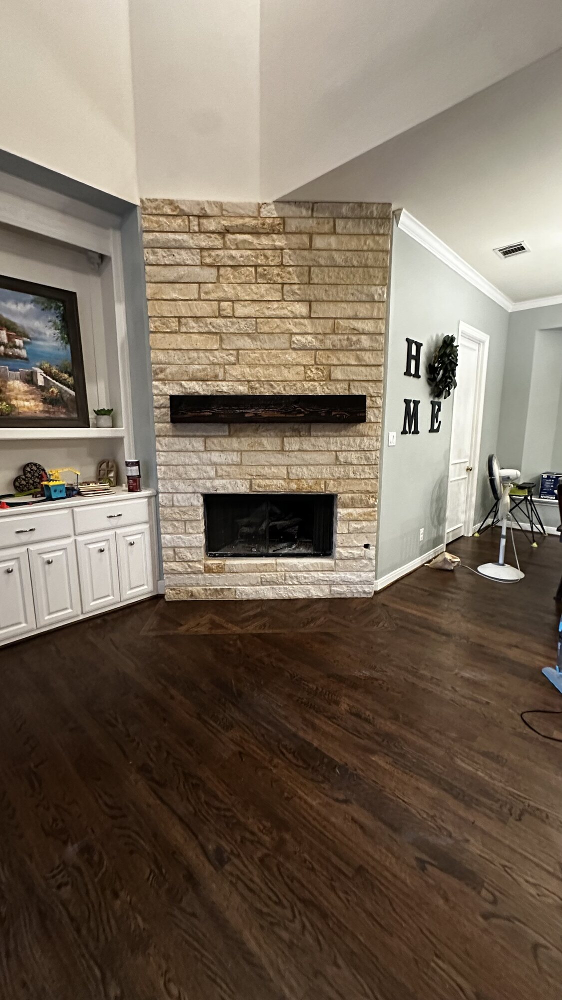 Front view of the completed fireplace renovation showing the finished stone chimney breast and dark wood mantel above the firebox