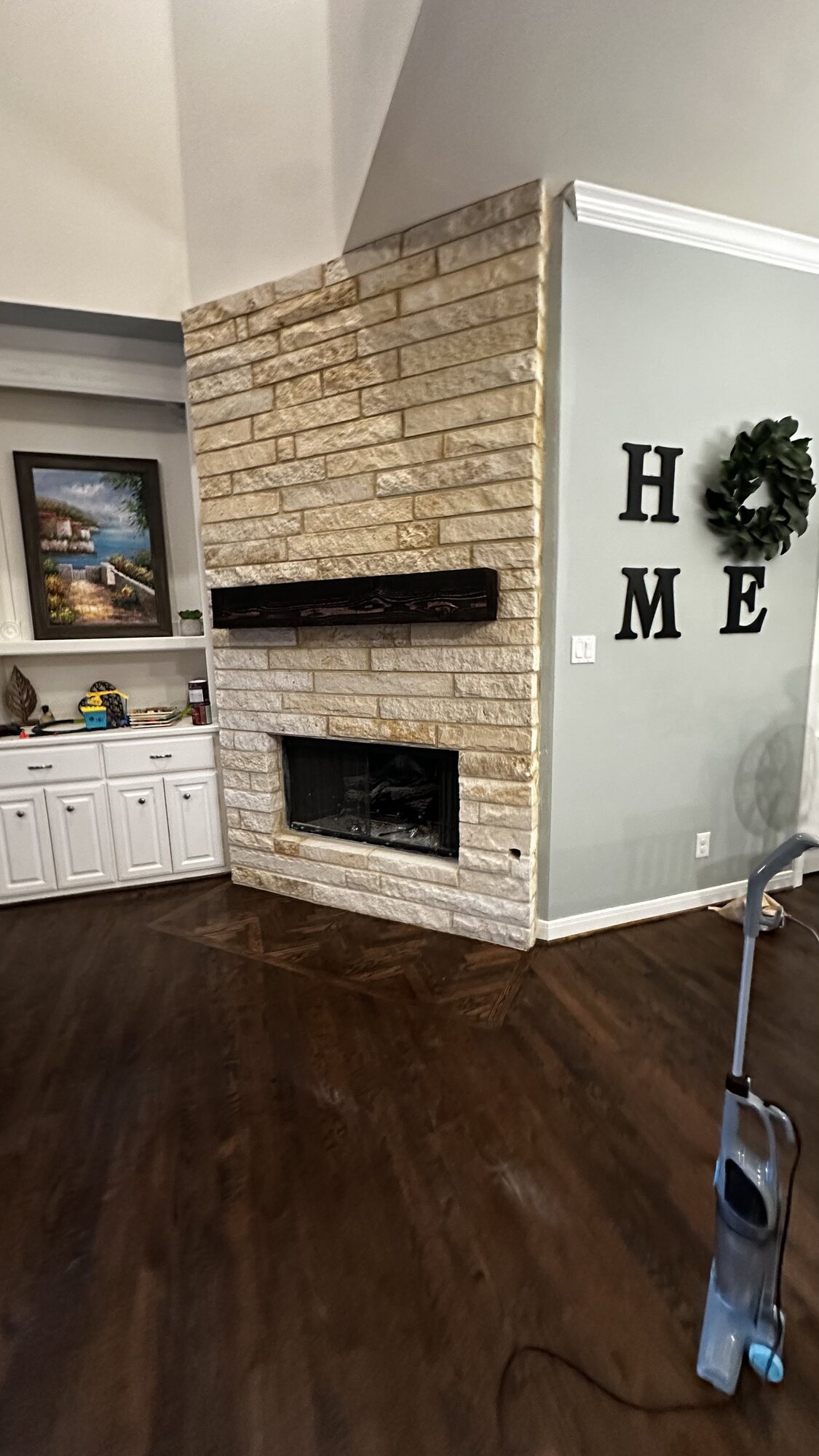 Completed fireplace renovation with a full-height stone surround and dark stained wood mantel in the finished living room