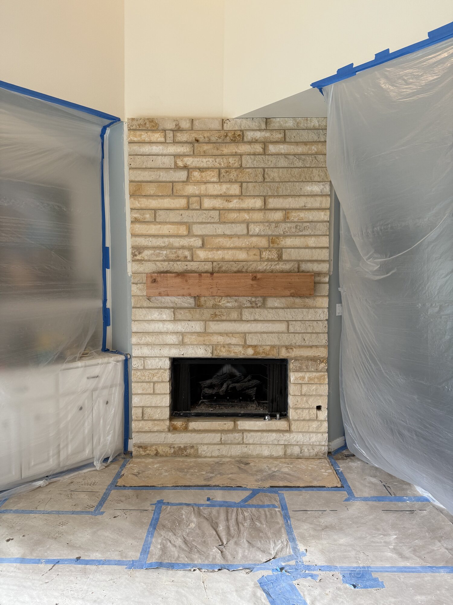 Closer view of the fireplace renovation in progress showing the extended stone veneer running to the ceiling and the unfinished mantel beam in place