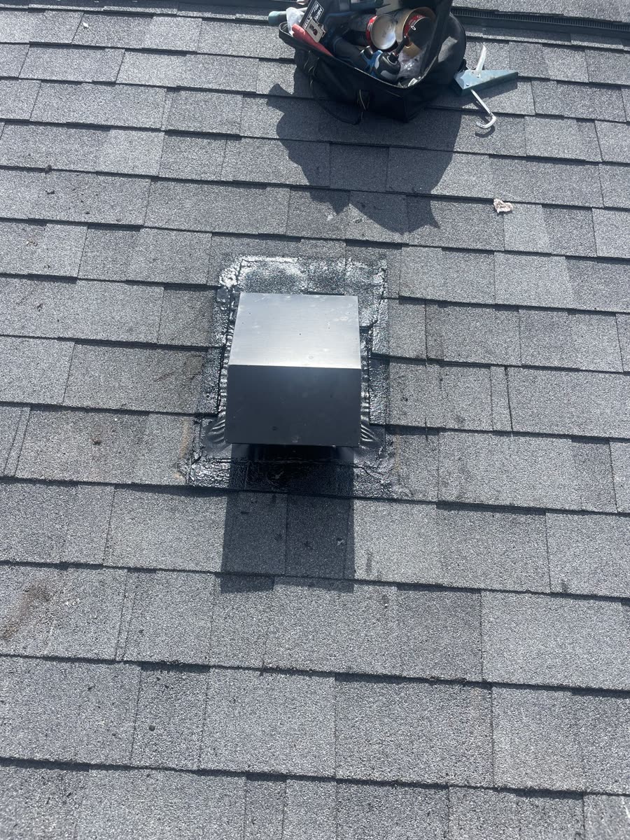 Rooftop dryer vent after service, showing the new vent cap sealed to the shingles from directly above